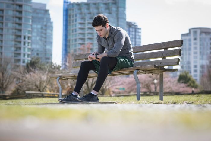 male Surface level of young man checking time while sitting on bench at park