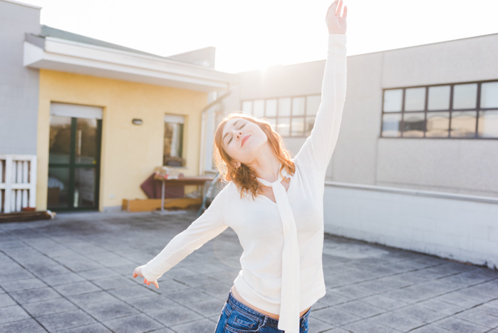 female Beautiful young woman dancing on sunlit roof terrace with eyes closed