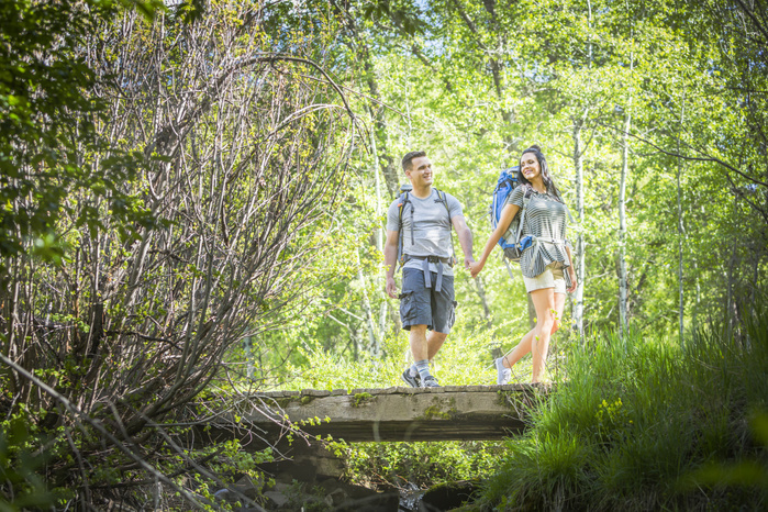 A couple hiking. Couple carrying backpacks across bridge in woods