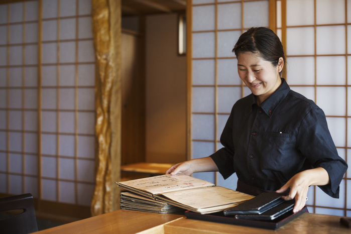 Smiling waitress standing at a counter in a Japanese sushi restaurant, holding menus. Smiling waitress standing at a counter in a Japanese sushi restaurant, holding menus.