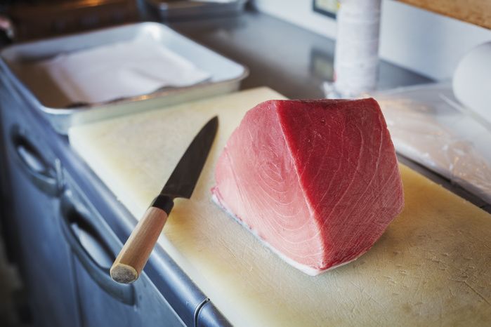 High angle close up of a fillet of tuna on chopping board  on counter at Japanese sushi restaurant. High angle close up of a fillet of tuna on chopping board  on counter at Japanese sushi restaurant.