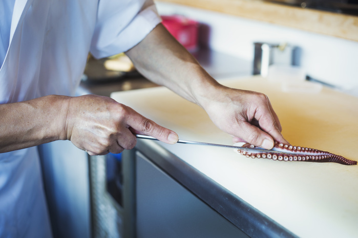 Close up of chef working at a counter at a Japanese sushi restaurant, slicing octopus tentacle. Close up of chef working at a counter at a Japanese sushi restaurant, slicing octopus tentacle.