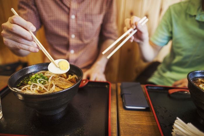 Two people, a Japanese man showing a Western man how to use chopsticks in a noodle shop. Two people, a Japanese man showing a Western man how to use chopsticks in a noodle shop.