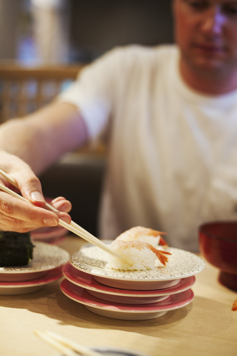 Close up of man sitting at table in Asian restaurant, picking up piece of sushi from a plate with chopsticks. Close up of man sitting at table in Asian restaurant, picking up piece of sushi from a plate with chopsticks.