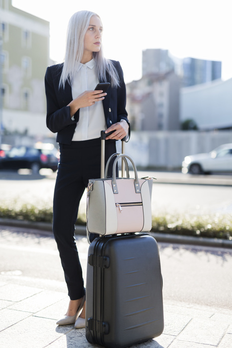 Young businesswoman in the city with cell phone and luggage