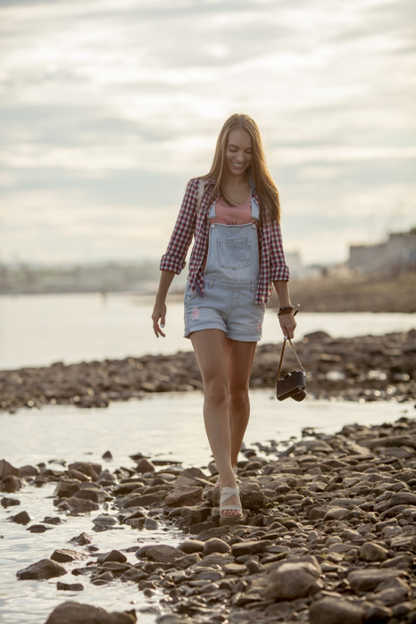female Young woman holding a camera walking on stony beach