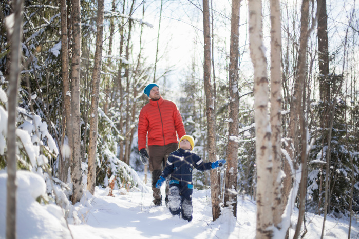 parent and child Man and son looking up while walking through snow covered forest