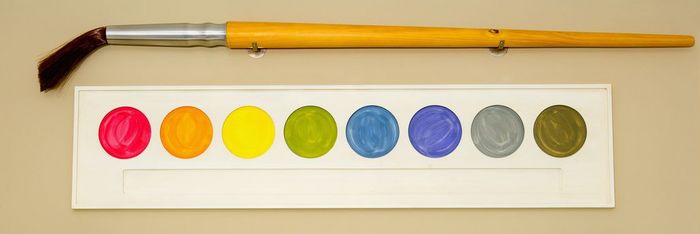 Palette of watercolor paints with a paintbrush mounted on a wall