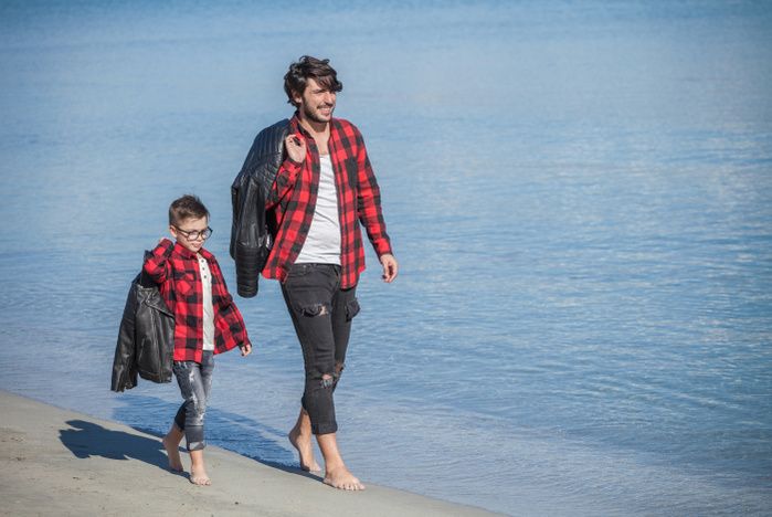 Father and son running along beach, carrying jackets over shoulder