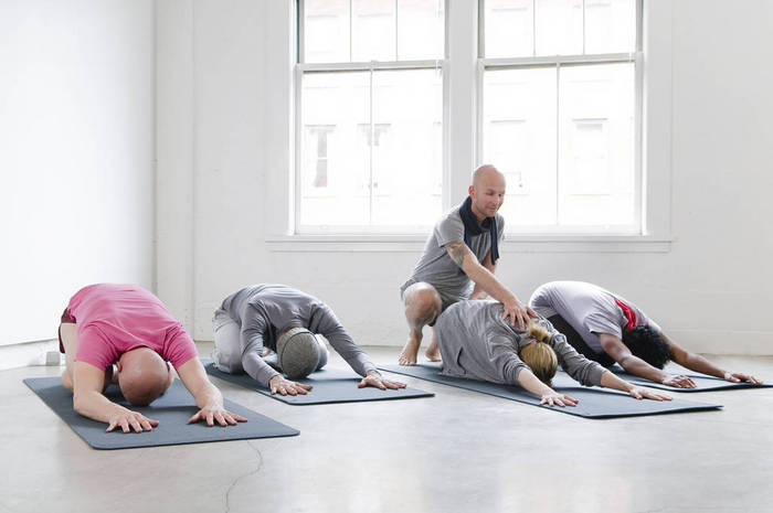 Student's stretch with instructor's help in yoga class, Vancouver, British Columbia