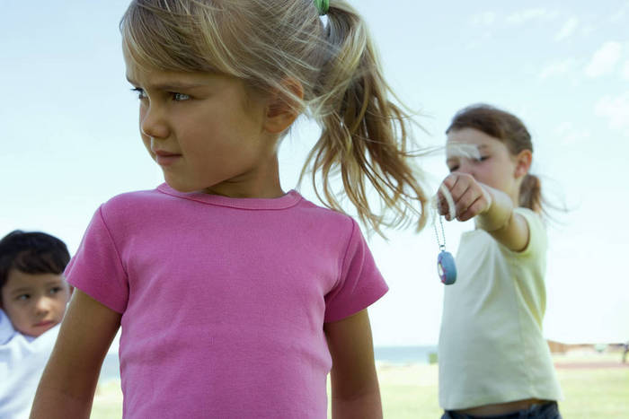 Three children outside, girl in foreground turning head while girl in background holds out toy to her