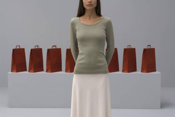 Woman standing in front of shopping bags, hands behind back, cropped view