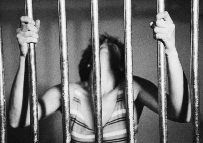 Woman behind prison bars with head back, b&w