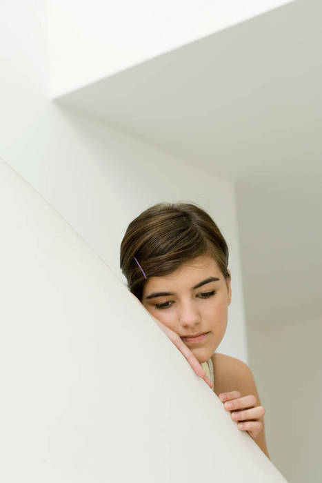 Teen girl leaning on edge of wall, looking down