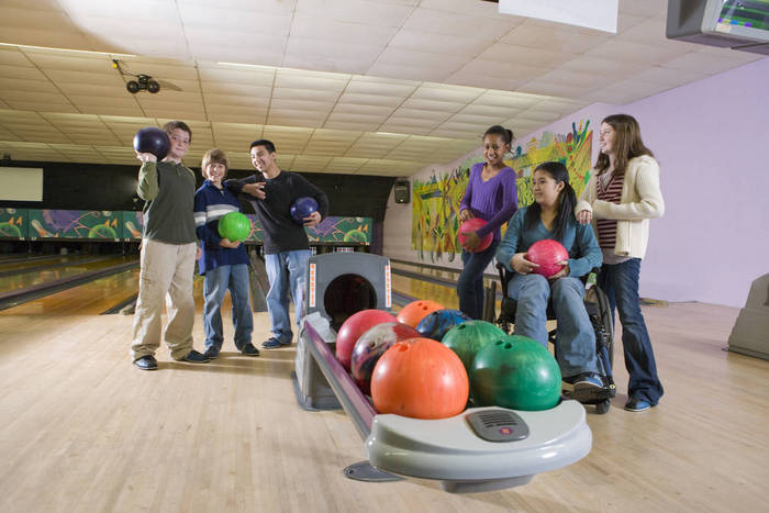 Portrait of multi-ethnic teenagers holding bowling balls and girl in wheelchair at bowling alley