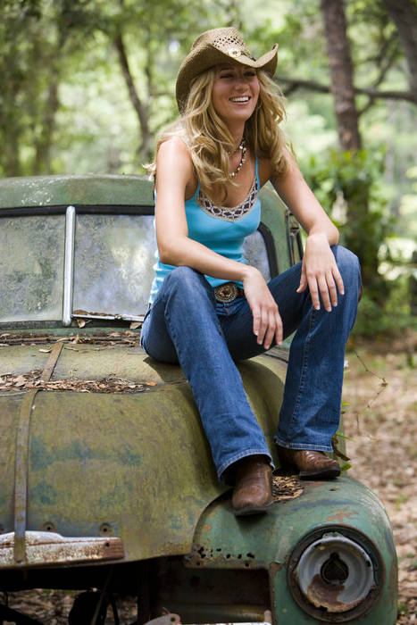 Young blonde cowgirl in cowboy hat sitting on vintage truck outdoors