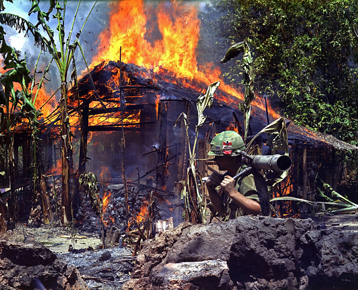 Vietnam war My Tho, Vietnam. A Burning Vietcong Base Camp. In the foreground is Private First Class Raymond Rumpa, St Paul, Minnesota, C Company, 3rd Battalion, 47th Infantry, 9th Infantry Division, with 45 pound 90mm recoiless rifle, 4 May 1968.