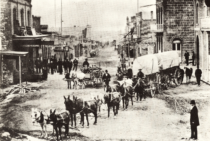 The main street of Helena, 1869, a typical town in the American West with a freight wagon drawn by mules in the foreground and signs for the local Saloon and Brewery further down the street.