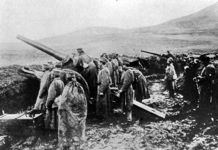 A Serbian heavy artillery battery, men standing in wet, muddy fortification, looking outwards in the same direction as the guns are pointing. Austro-Hungary invaded Serbia in July 1914.