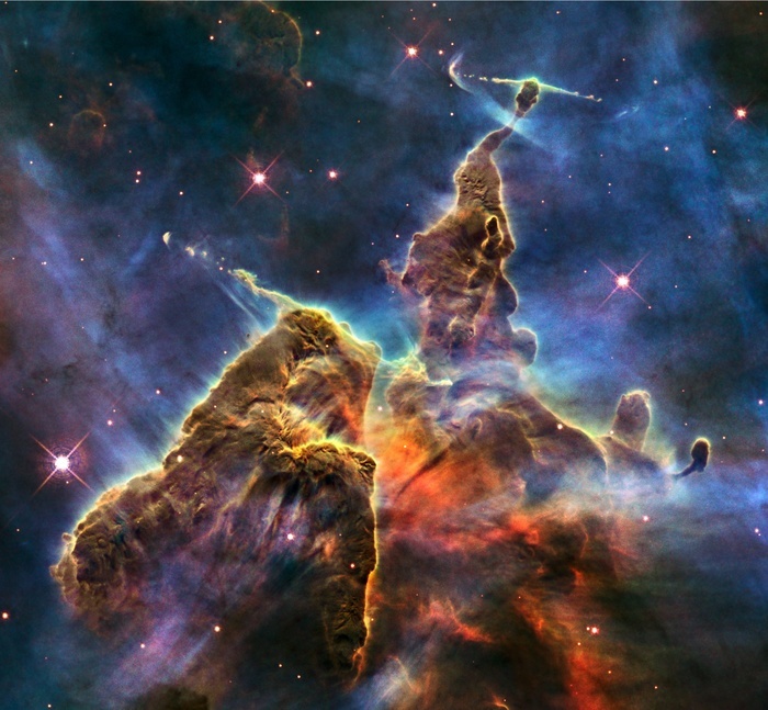 Hubble photo of a small portion of one of the largest known star-birth regions in the galaxy, the Carina Nebula. Three light-year-tall towers of cool hydrogen laced with dust rise from the wall of the nebula. Scorching radiation and fast winds (streams of charged particles) from super-hot newborn stars in the nebula are shaping and compressing. Scorching radiation and fast winds (streams of charged particles) from super-hot newborn stars in the nebula are shaping and compressing the pillar, causing new stars to form within it. Streamers of hot ionized gas can be seen flowing off the ridges of the structure The denser parts of the pillar are resisting The denser parts of the pillar are resisting being eroded by radiation much like a towering butte in Utah's Monument Valley withstands erosion by water and wind.