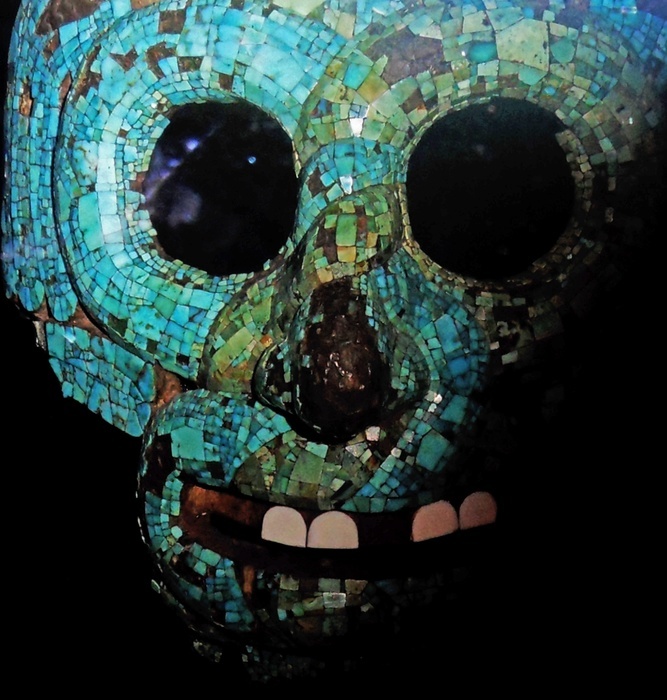 Turquoise mosaic mask AD 1400-1521.  A pair of serpents is entwined around the eyes, nose and mouth of this mask.  Two serpent tails meet at the top and a feathered plume hangs down on either side.  Snakes were used metaphorically to represent the attributes of two well-known Aztec deities : The Rain God Tlaloe and the Creator God Quetzalcoatl.