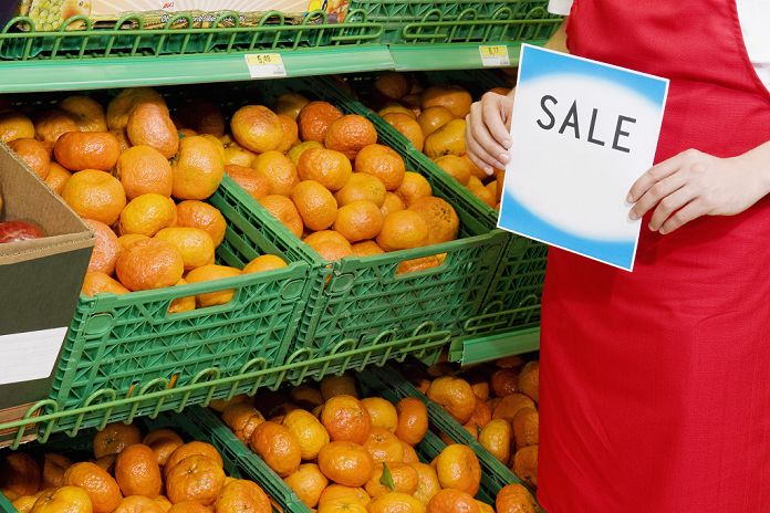 Sales clerk showing placard near crates of oranges