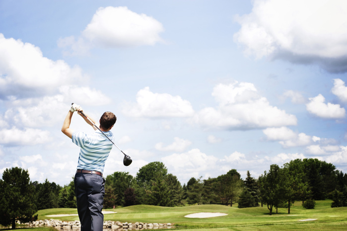 Golfer Watching Ball After Drive Rear view of man swinging golf club against cloudy sky