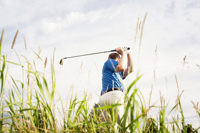 Golfer through long grass Rear view of man playing golf on field against sky