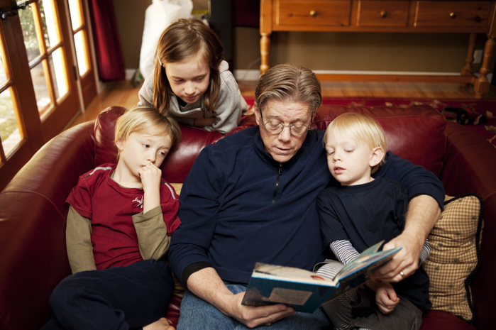 grandfather reading book to grandchildren High angle view of grandfather telling stories to children while sitting on sofa at home