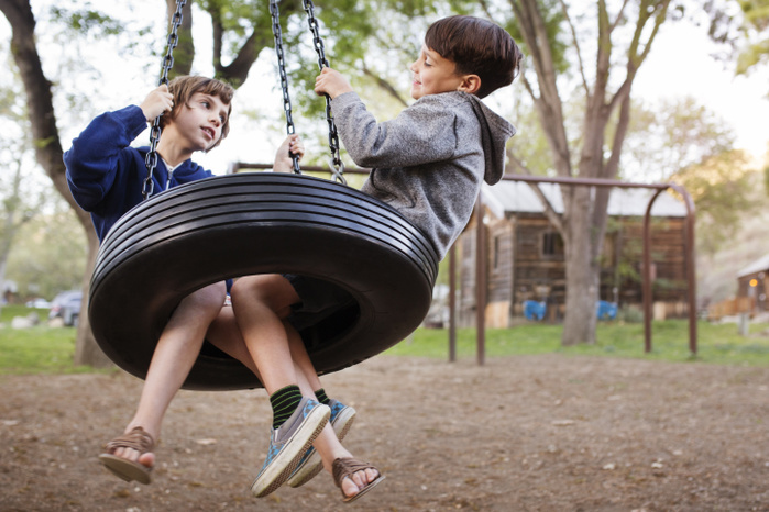 Side view of siblings sitting on tire swing at park