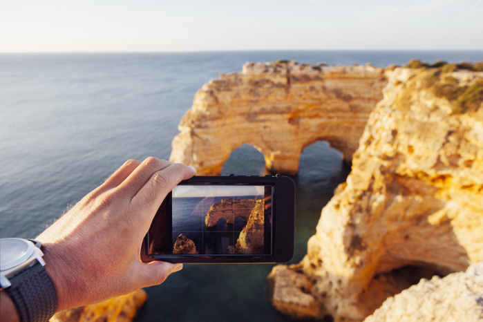 Cropped image of man photographing natural arch through phone at Praia da Marinha