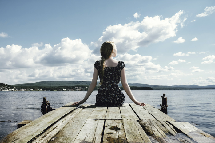 Thoughtful woman sitting on pier over river against cloudy sky
