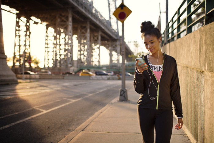 Female jogger text messaging while walking on sidewalk