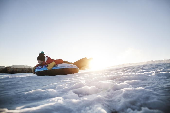Man snowtubing on mountain against clear sky during sunny day