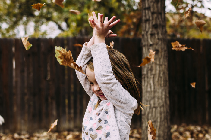 Cheerful girl playing with dry leaves at park during autumn