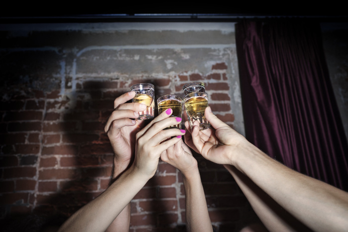 Cropped image of friends toasting tequila shots against brick wall