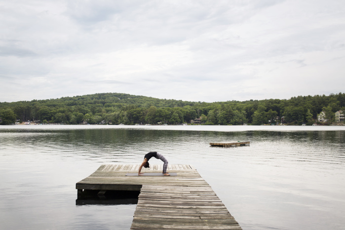 Woman exercising on pier over lake against sky