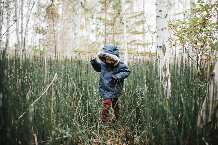 Boy wearing hooded jacket while playing amidst forest