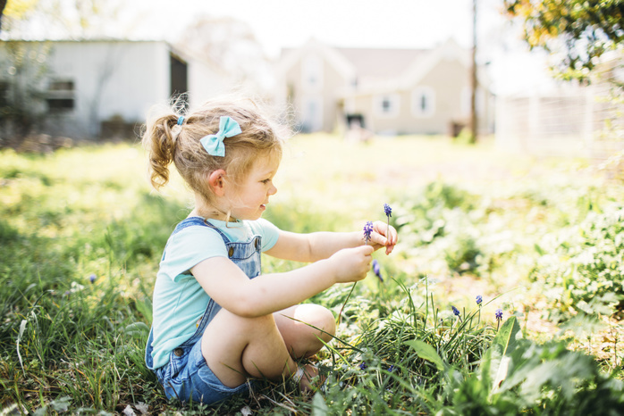 FinleyMarieHicks2017 Girl playing with flowers while sitting on grassy field at backyard