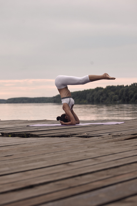 Side view of woman practicing headstand on pier by lake against cloudy sky during sunset