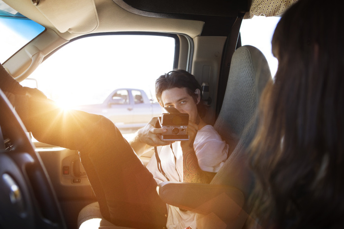 Man photographing woman through instant camera while sitting in camper van