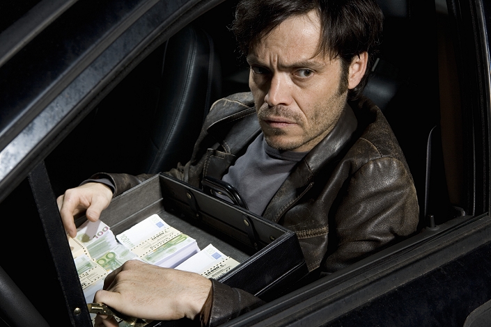 A man sitting in a car with an open briefcase full of money