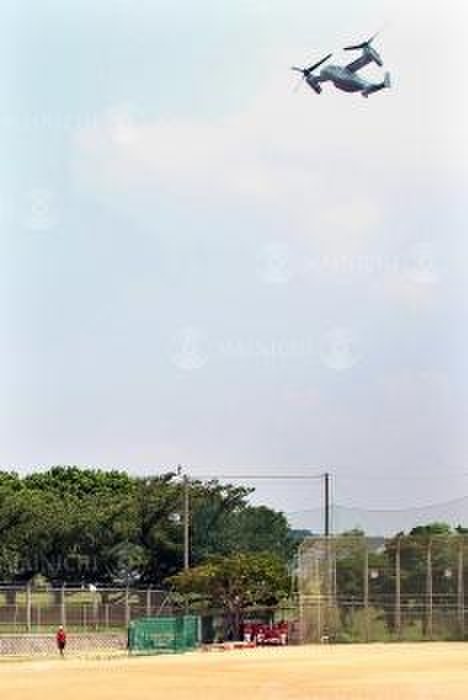 Osprey flying over Futenma Daini Elementary School, Okinawa An Osprey flies overhead, even when baseball is being played in the schoolyard, at Futenma No. 2 Elementary School in Ginowan, Okinawa, July 26, 2018, 3:28 p.m. Photo by Hiroshi Higa