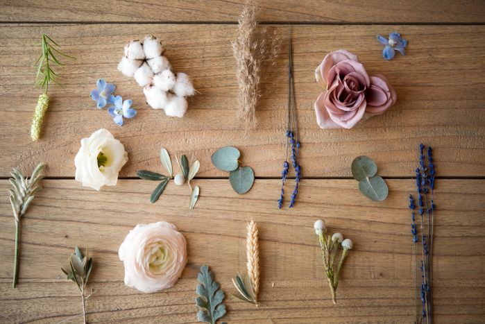 Still life of pastel coloured flower heads, flower stems and leaves on wood, overhead view