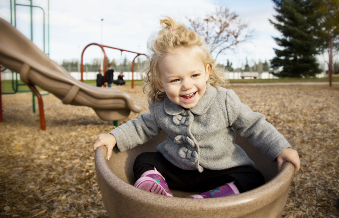 A cute young girl spinning in a saucer on a playground during the fall season; Spruce Grove, Alberta, Canada