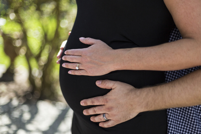 A couple expecting a baby, standing with hands on her pregnant belly; Surrey, British Columbia, Canada