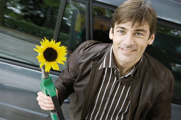 Man at gas station holding gas nozzle with sunflower emerging from end